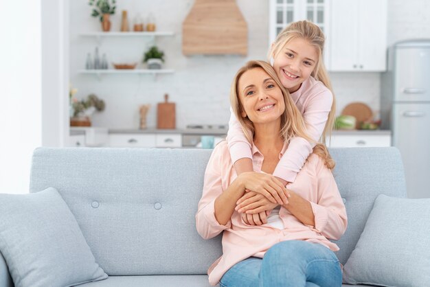 Mother sitting on sofa and embraced by daughter