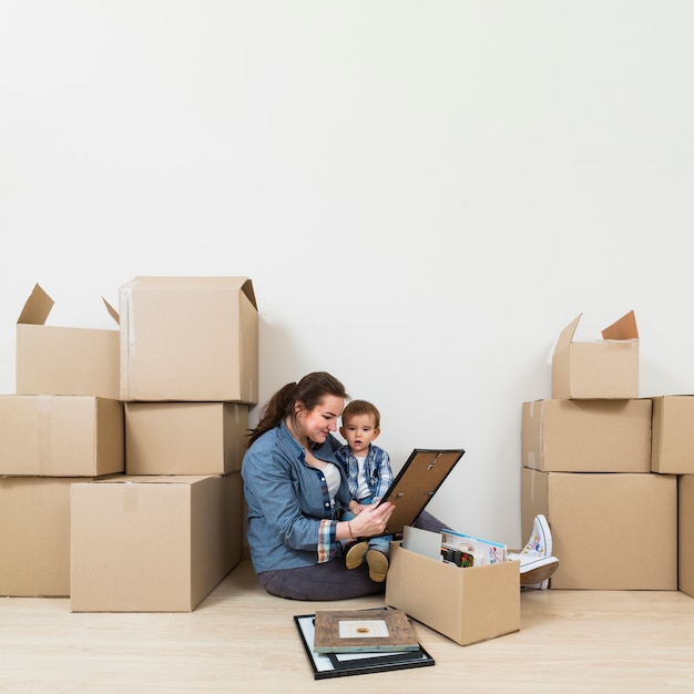 Free photo mother sitting with her son looking at picture frame unpacking the cardboard boxes