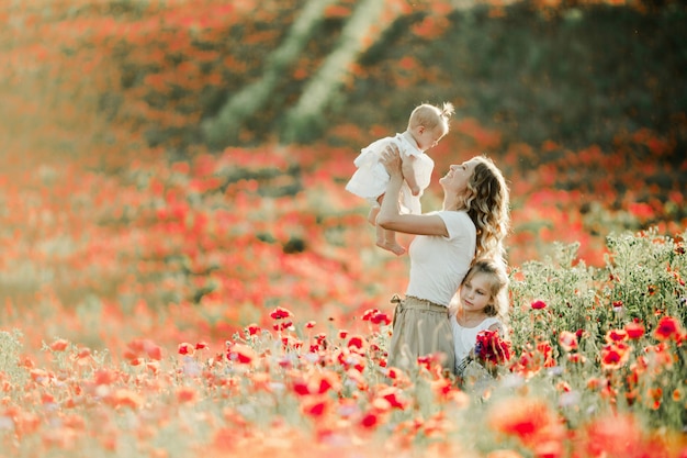 Mother smiles to her baby, elder daughter nestles to mom on the poppy field