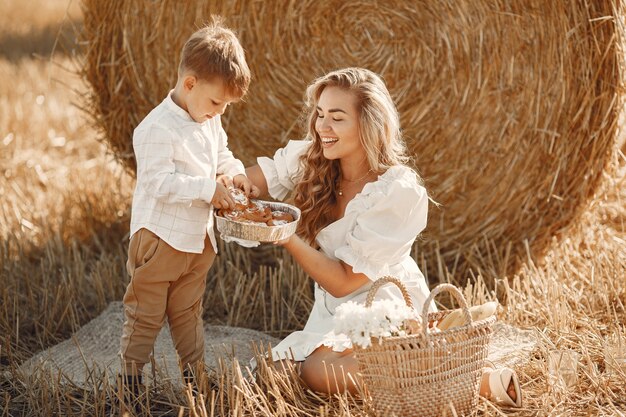 Mother and son. Hay stack or bale on yellow wheat field in summer. Children having fun together.