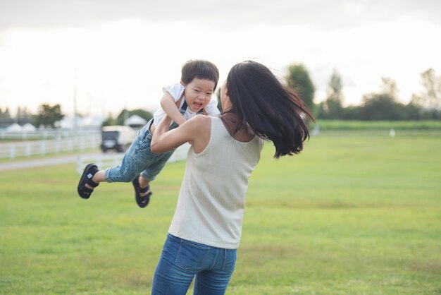 Mother and son playing in the park at the sunset time. people having fun on the field. concept of friendly family and of summer vacation.
mother throwing his son in the air.