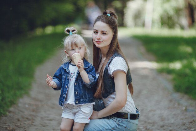 Mother squatting with her daughter while eating an ice cream with defocused background