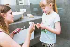 Free photo mother squeezing paste on toothbrush of daughter