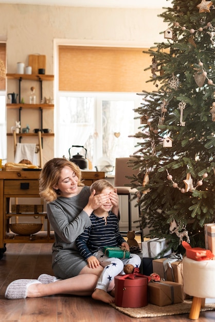 Mother surprising boy with gift next to christmas tree