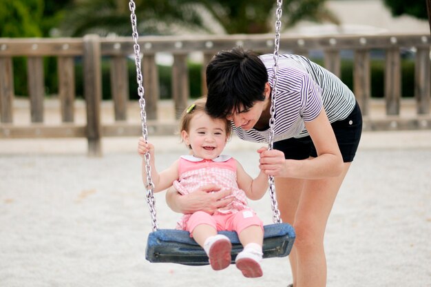 Mother swinging her little daughter on a swing in a playground