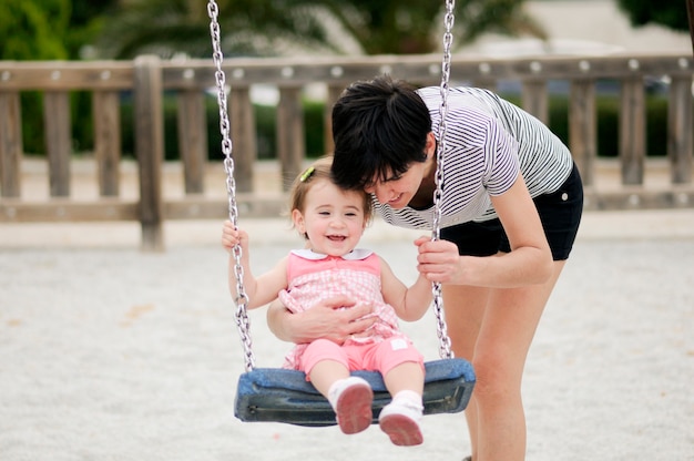 Mother swinging her little daughter on a swing in a playground