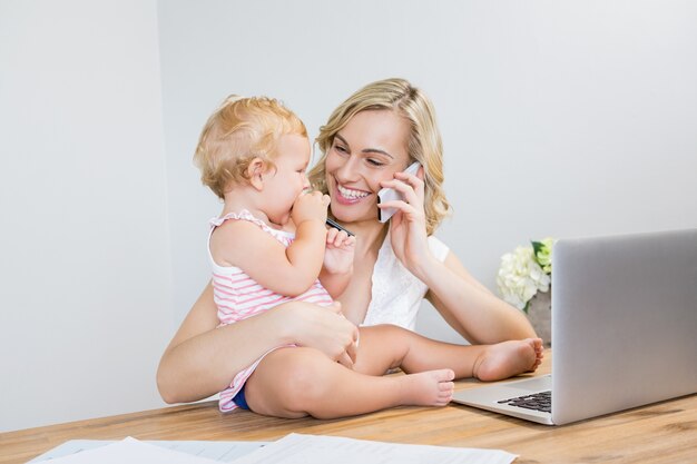 Mother talking on mobile phone while holding her baby girl