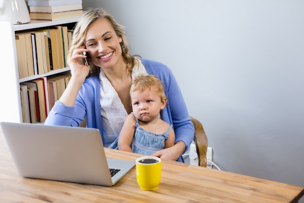 Mother talking on mobile phone with baby on her lap