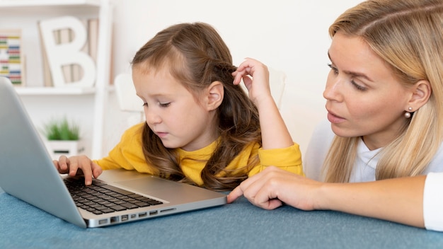Mother teaching her daughter how to use laptop
