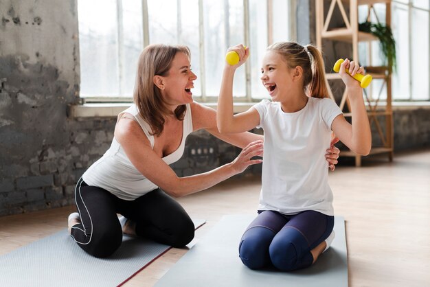 Mother tickling daughter holding weights on yoga mat