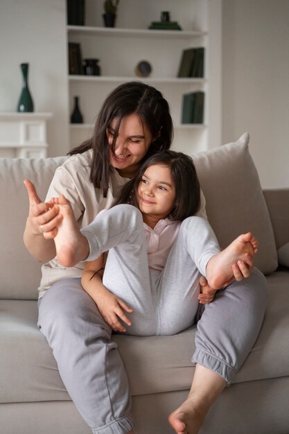 Mother tickling kid on couch full shot