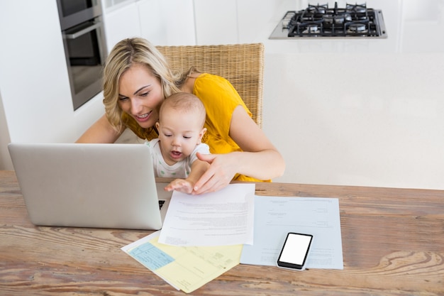 Mother using laptop with baby boy in kitchen