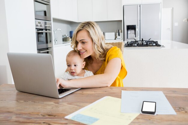 Mother using laptop with baby boy in kitchen