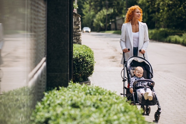 Free photo mother walking by the house with her little son in a baby carriage