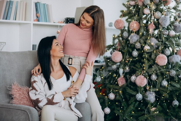 Mother with adult daughter with christmas presents by christmas tree