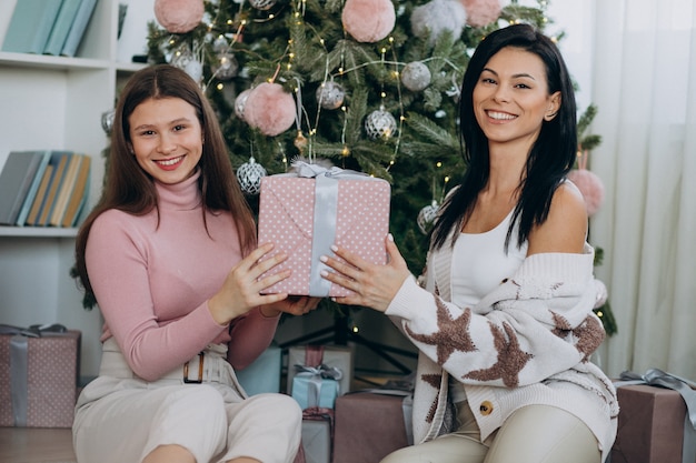 Mother with adult daughter with christmas presents by christmas tree