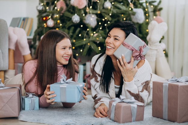 Mother with adult daughter with christmas presents by christmas tree