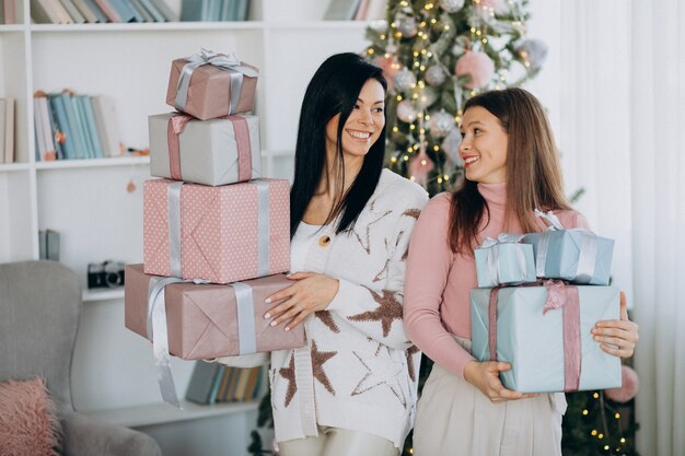 Mother with adult daughter with christmas presents by christmas tree