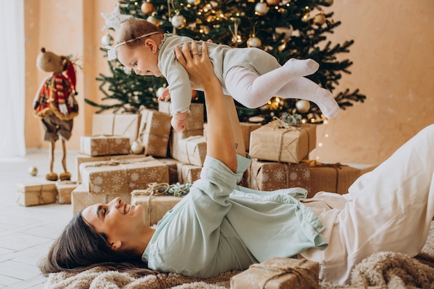 クリスマスツリーのそばに横たわっている赤ん坊の娘を持つ母