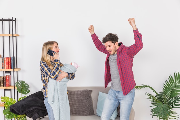 Mother with baby talking on phone near cheerful father 