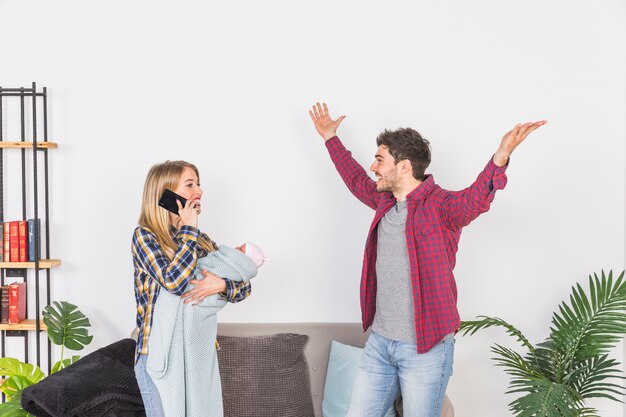 Mother with baby talking on phone near happy father 