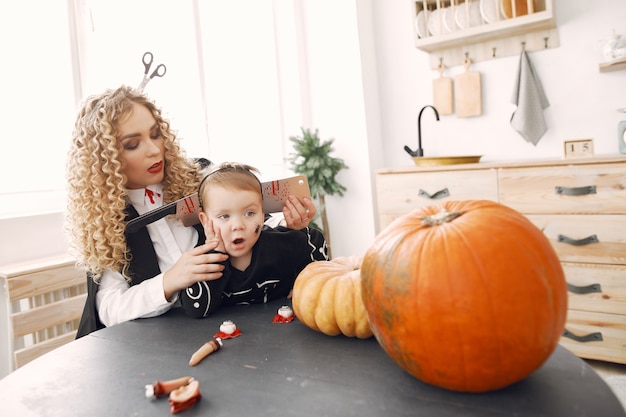 Mother with child in costumes and makeup. Family prepare to celebration of Halloween.