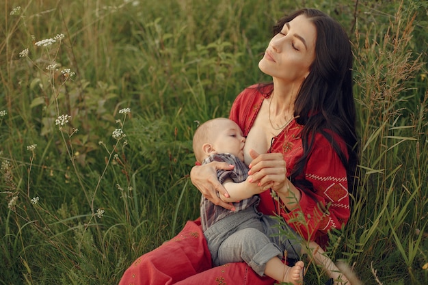 Mother with cute daughter. Mom breastfeeding her little son. Woman in a red dress.