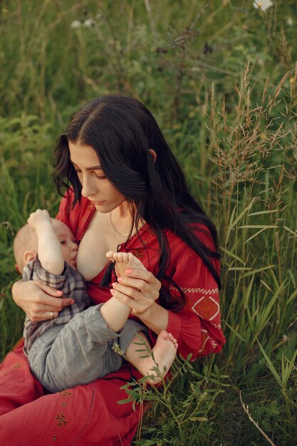 かわいい娘を持つ母。彼女の幼い息子を母乳で育てるママ。赤いドレスを着た女性。