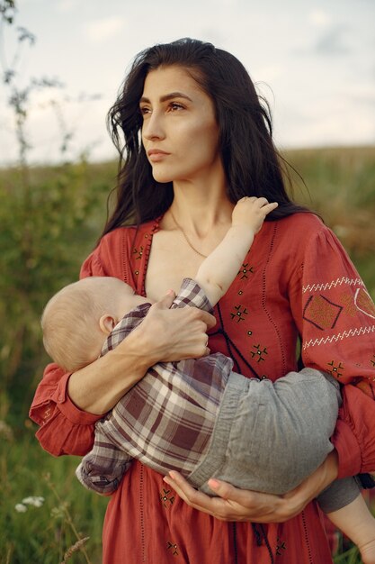 かわいい娘を持つ母。彼女の幼い息子を母乳で育てるママ。赤いドレスを着た女性。