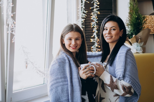 Mother with daughter drinking tea together at the kitchen by the window