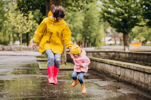 Mother with daughter having fun jumping in puddles