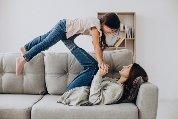 Mother with daughter having fun together at home on sofa