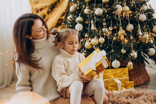 クリスマスツリーの下でクリスマスプレゼントを保持している娘と母