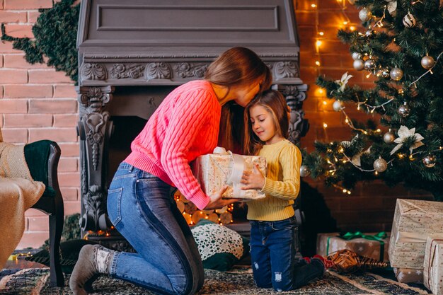 クリスマスの暖炉のそばでプレゼントを梱包の娘を持つ母