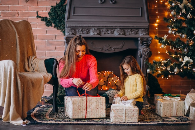 Мать с дочерью, упаковка подарок у камина на Рождество