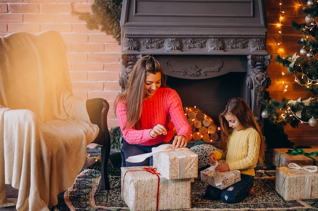 クリスマスの暖炉のそばでプレゼントを梱包の娘を持つ母