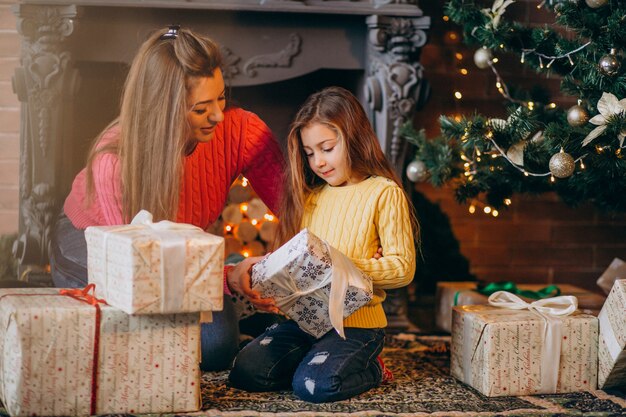 クリスマスの暖炉のそばでプレゼントを梱包の娘を持つ母