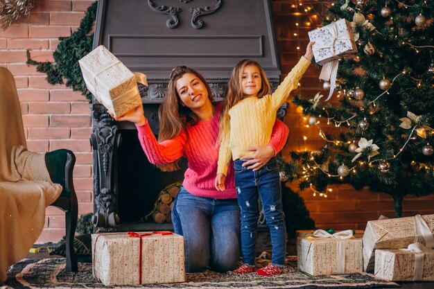 Мать с дочерью, упаковка подарок у камина на Рождество