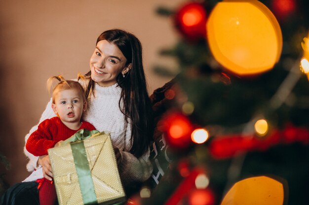 クリスマスツリーのそばに座っている娘を持つ母