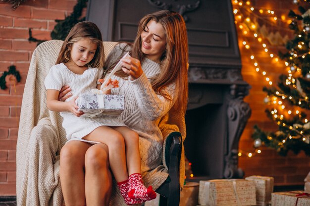 Mother with daughter sitting in chair by Christmas tree