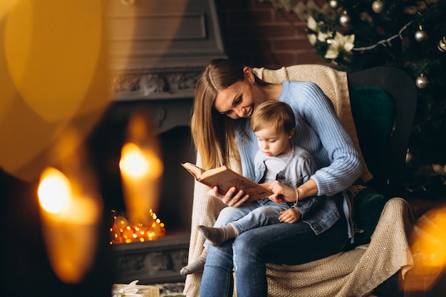 Free photo mother with daughter sitting in chair by christmas tree