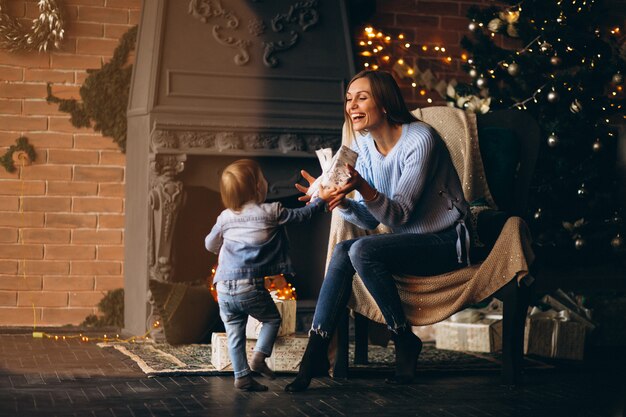 Mother with daughter sitting in chair by Christmas tree