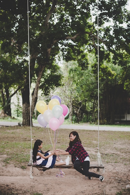 一緒に屋外でリラックスした風船のカラフルでブランコに座っている娘を持つ母。