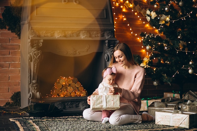 Mother with daughter unpacking christmas presents by Christmas tree