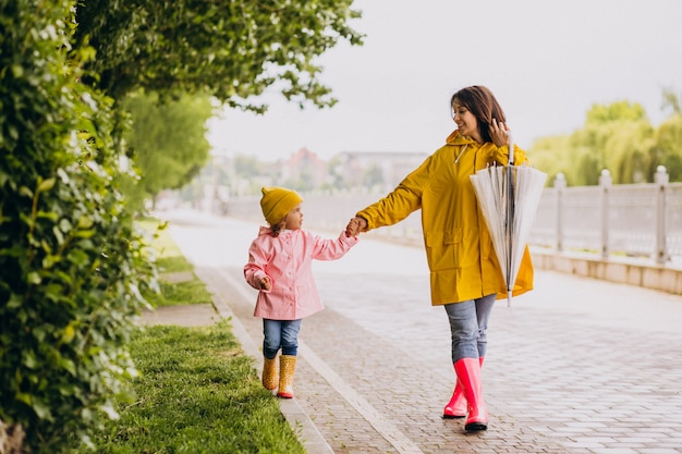 Madre con la figlia che cammina nel parco sotto la pioggia che indossa stivali di gomma