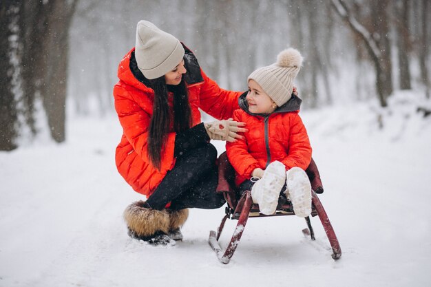 Mother with daughter in winter park sledging
