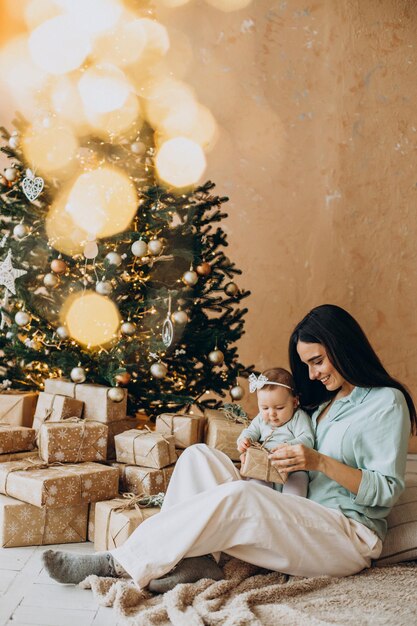 Mother with her baby daughter with gift boxes by the Christmas tree