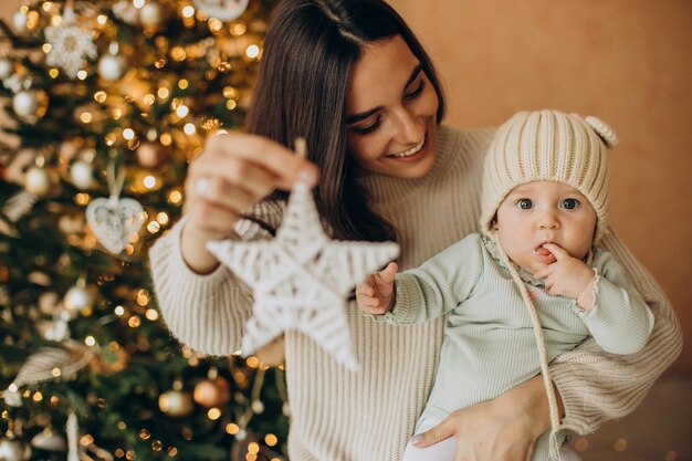 Mother with her daughter holding christmas toy by the christmas tree