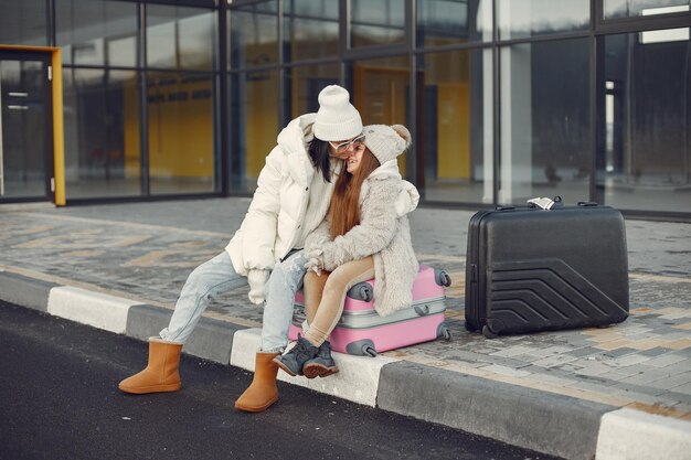 Mother with her daughter sitting outdoors on a luggage and waiting for travel