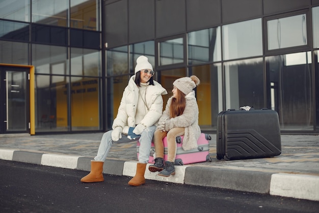 Mother with her daughter sitting outdoors on a luggage and waiting for travel